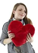 Beautyful Young And Smiling Woman Embraces Heart Shaped Pillow With Her Hands