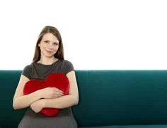 Beautyful Young And Smiling Woman Sitting On A Sofa Embracing Heart Shaped Pi