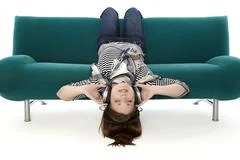 Beautiful Young Smiling Woman Lying On A Sofa And Listens To Music With Headp