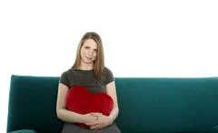 Beautyful Young Woman Smiling And Sitting On A Sofa With Heart Shaped Pillow 