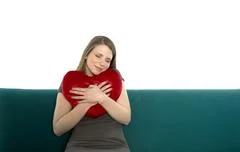Beautyful Young And Smiling Woman Sitting On A Sofa Embracing Heart Shaped Pi