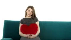 Beautyful Young Woman Smiling And Sitting On A Sofa With Heart Shaped Pillow 